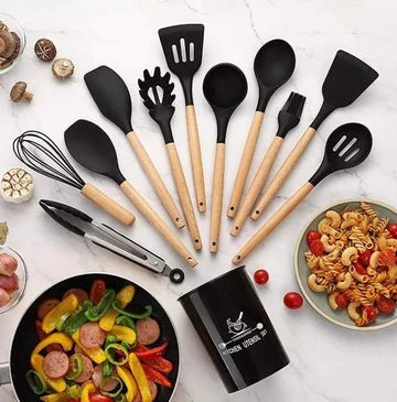 Set of black and wooden kitchen utensils on a white surface with food items.