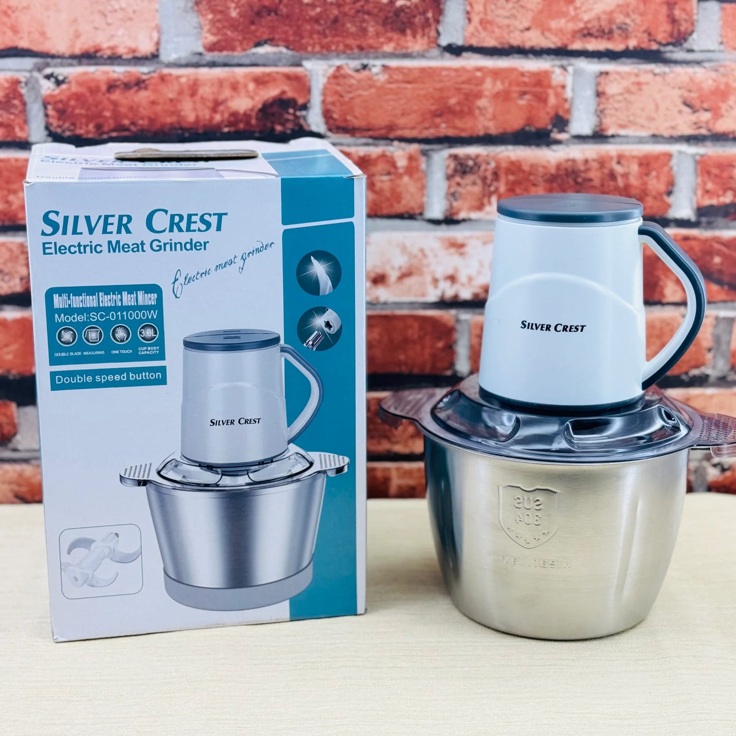 Silver Crest electric meat grinder with packaging against a brick wall background
