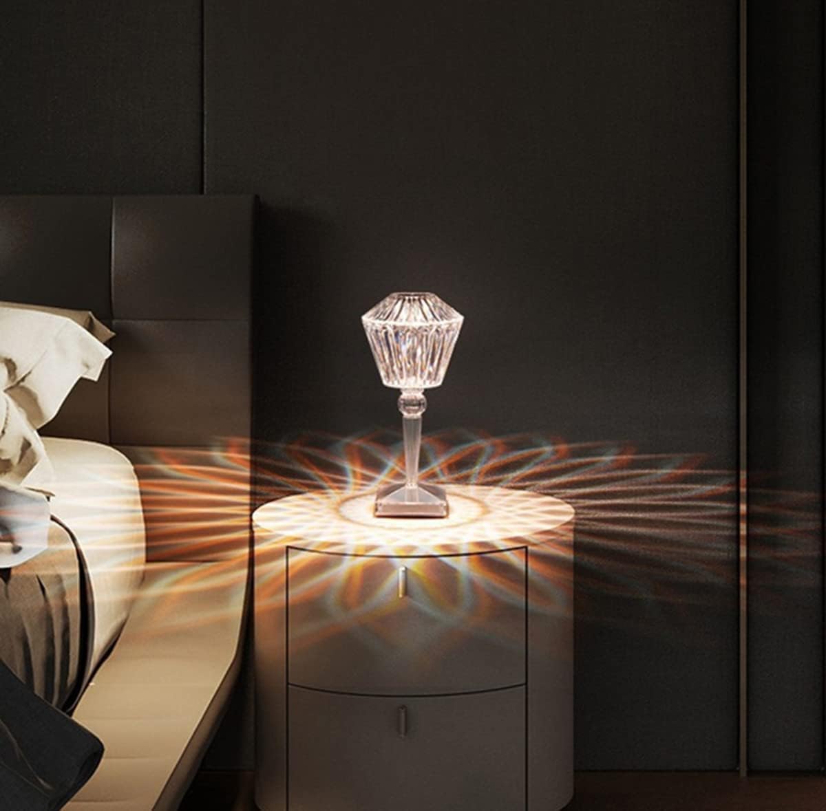 Decorative crystal lamp on a nightstand with a dark wall and bed in the background