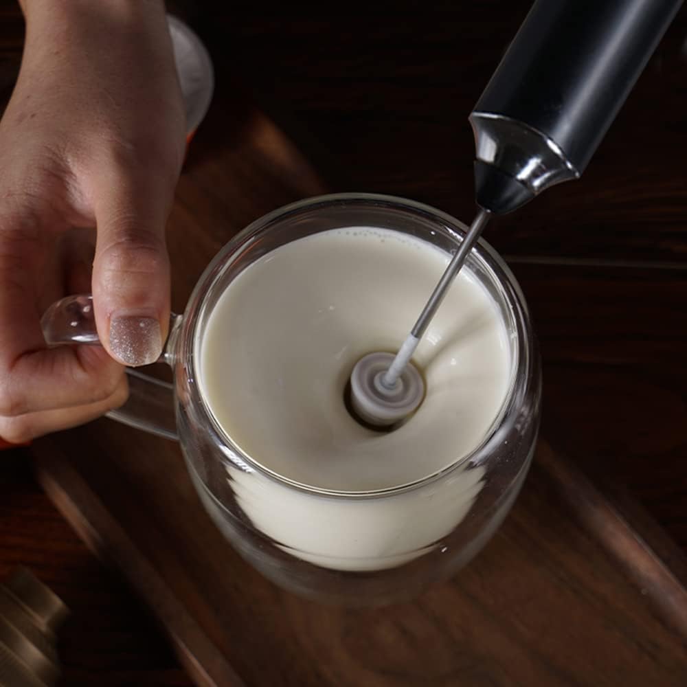 Person using a milk frother to froth milk in a glass mug