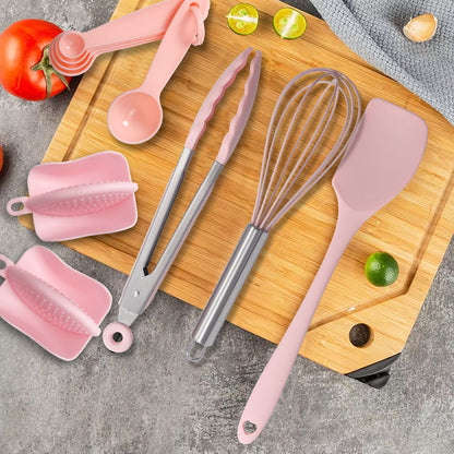 Set of pink kitchen utensils including tongs, whisk, and spatula on a wooden cutting board with vegetables.