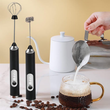 Two black handheld milk frothers next to a white teapot and a glass of coffee with cream being poured.